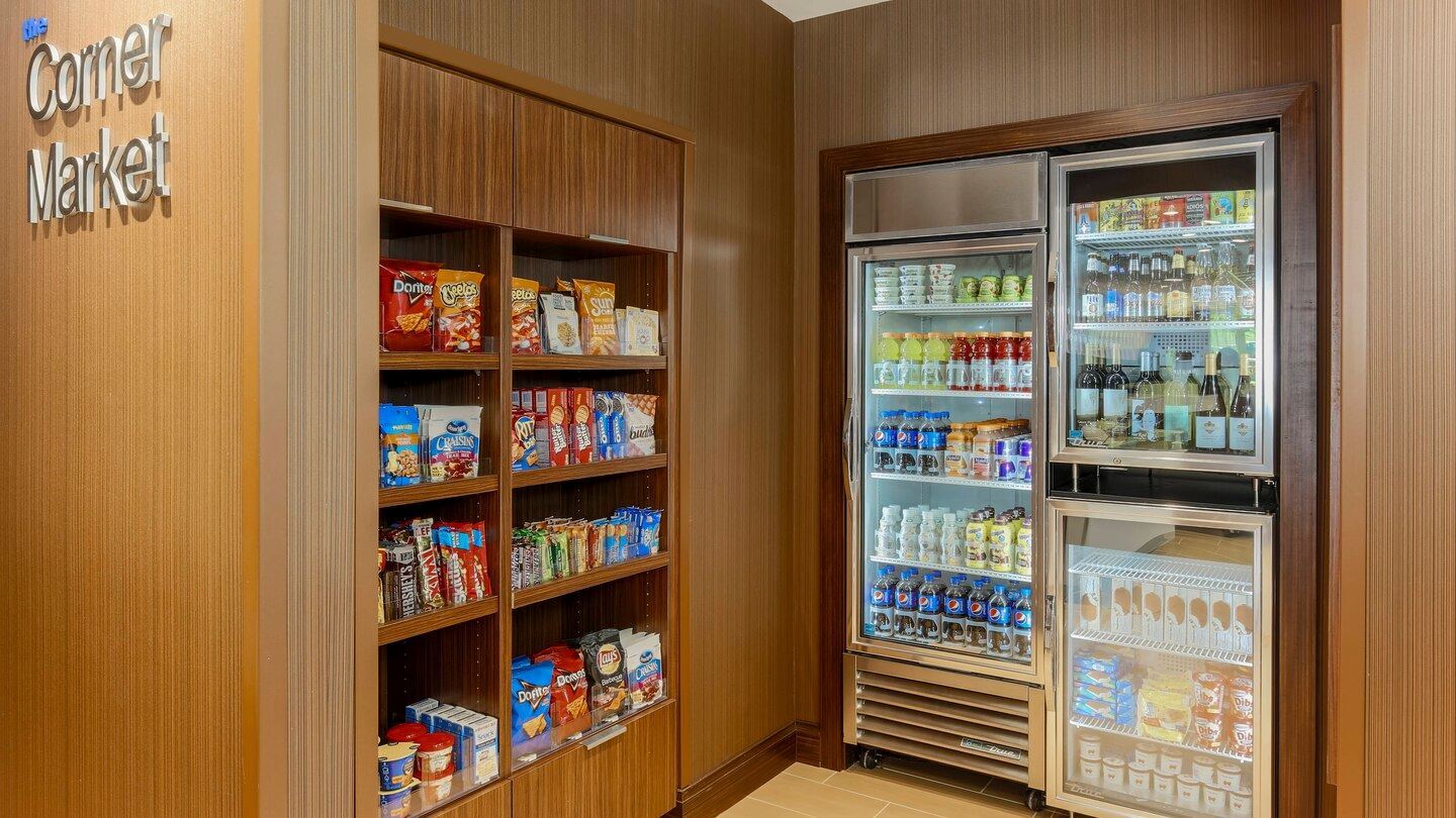 Corner market in the hotel that has various shelves with differnt snacks and two fridges of drinks a