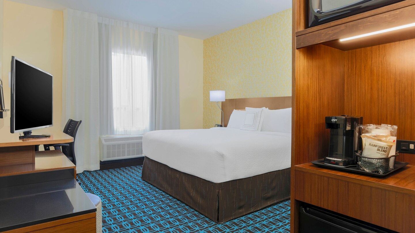 One white comforter King Bed with teal and brown carpemt and complimentary amenities 